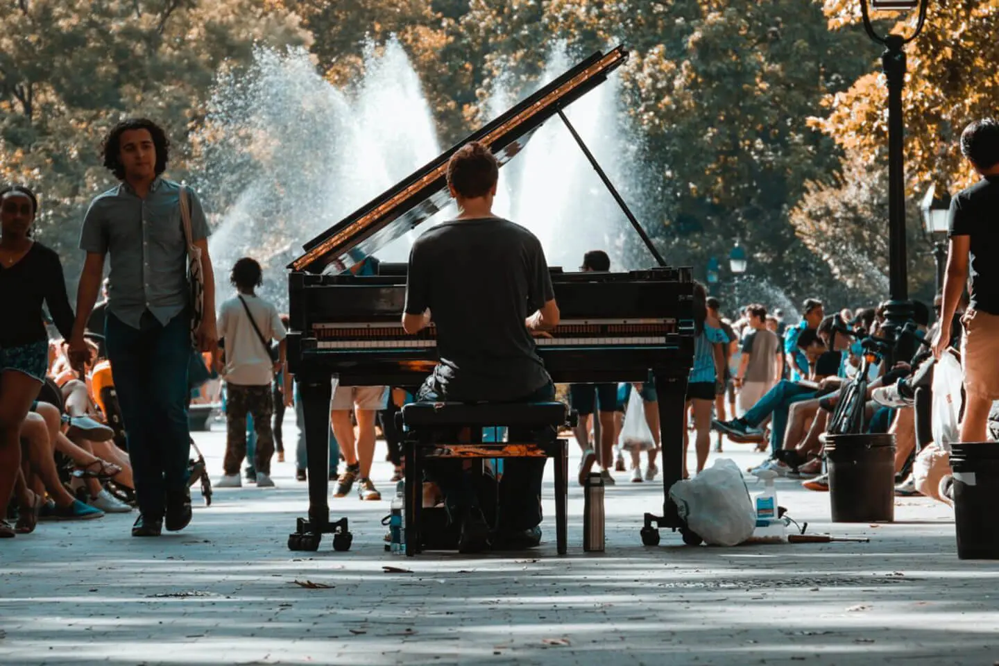 Man playing piano outdoors in a Manhattan park with onlookers in the background.