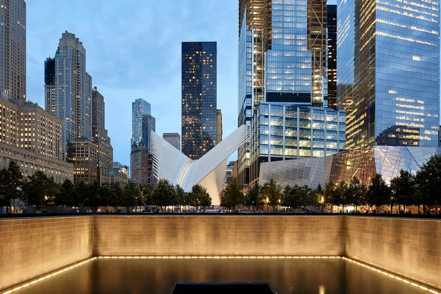 Evening view of an urban plaza with the oculus structure at the World Trade Center amidst surrounding skyscrapers in Manhattan, New York City.