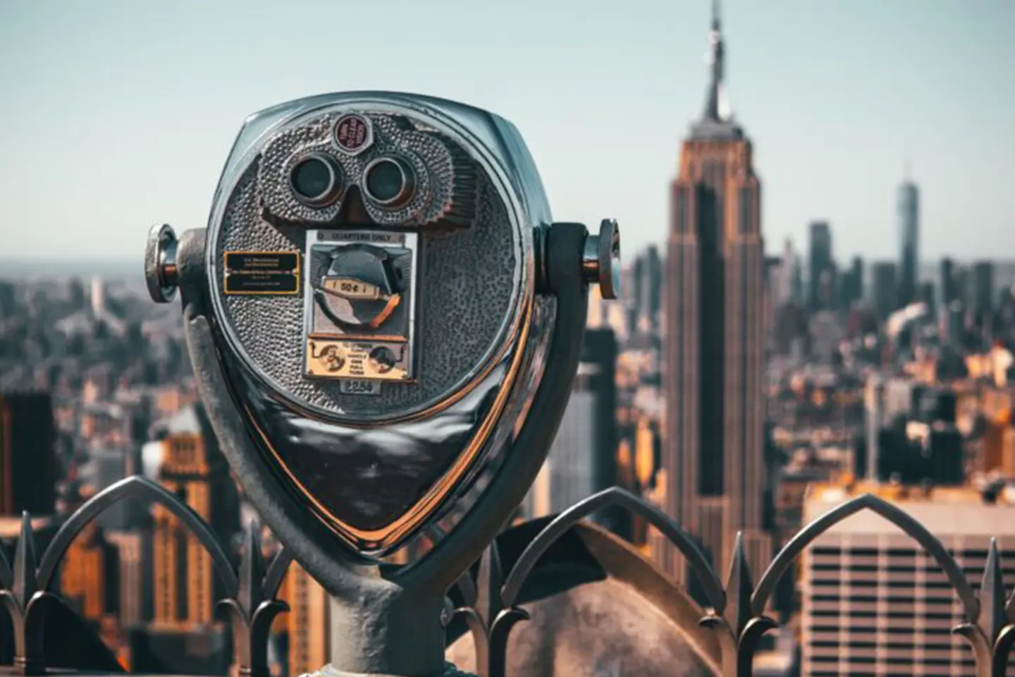 Coin-operated binoculars overlooking a cityscape with Manhattan skyscrapers.