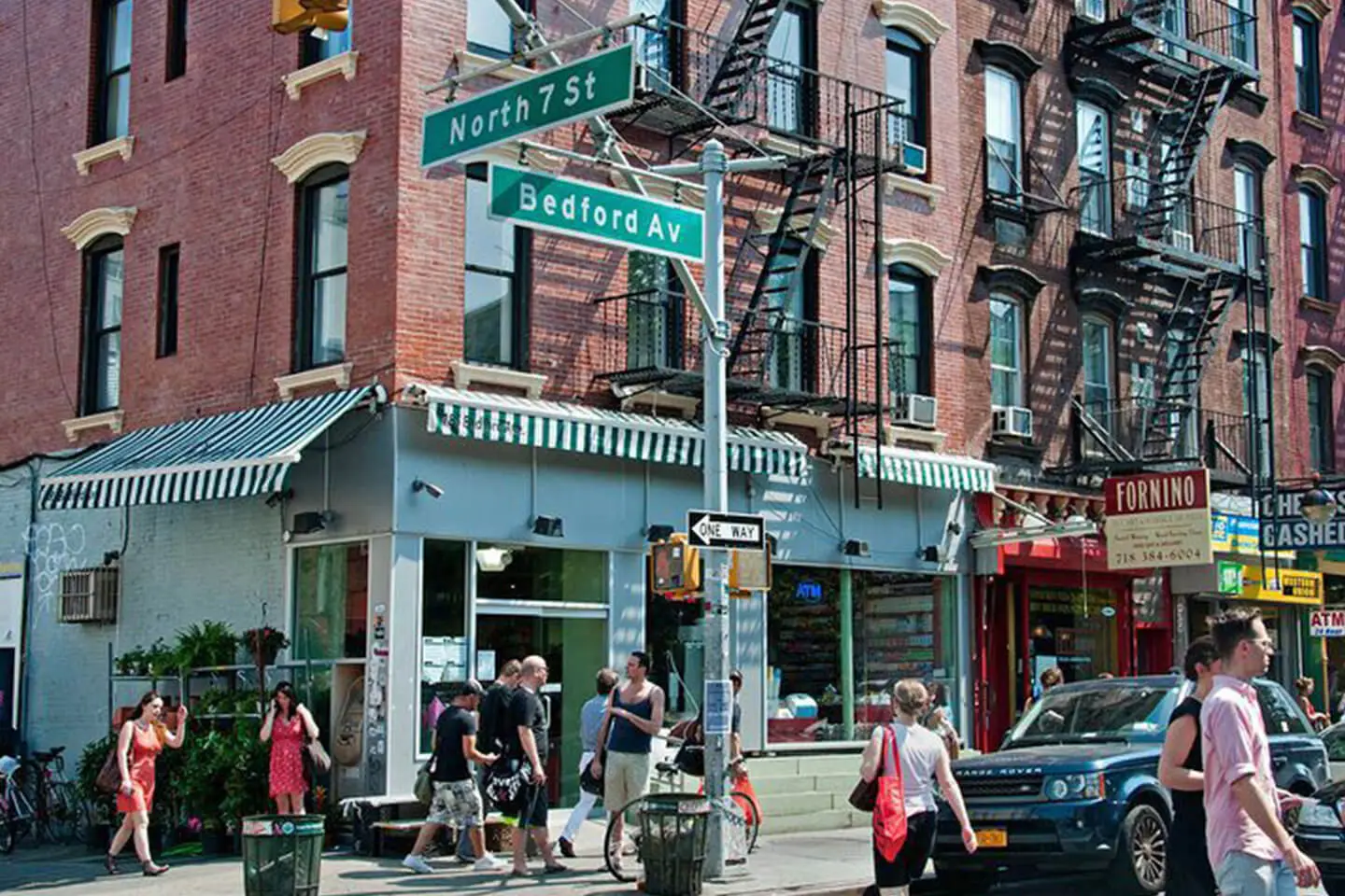 Street corner in an urban neighborhood in Manhattan with pedestrians, brick buildings, and a street sign for north 7 st and bedford ave.