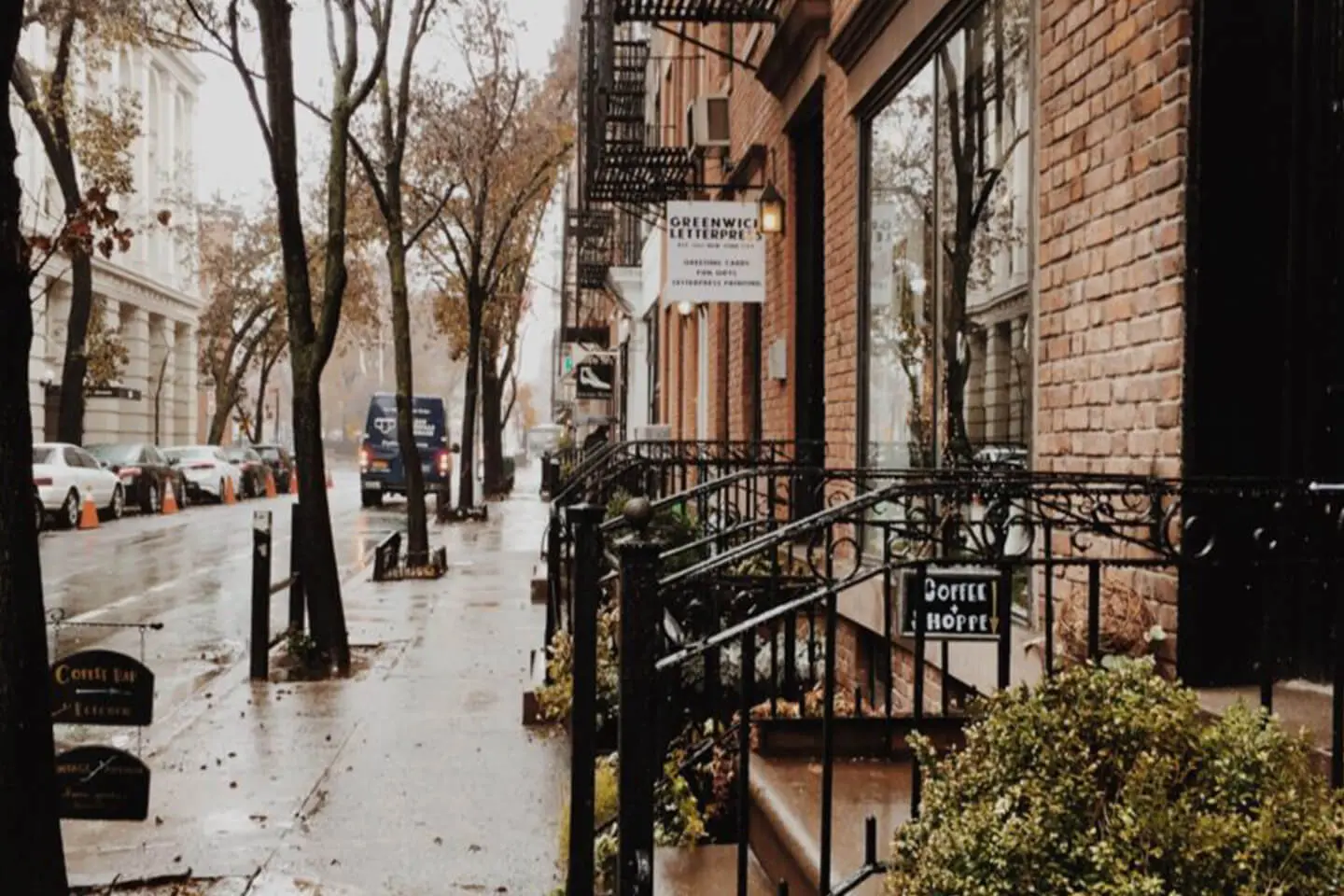 A rainy day on a Manhattan city street with wet sidewalks, bare trees, and a coffee shop's entrance.