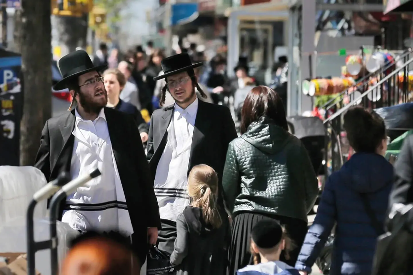 Two men in traditional Jewish attire talking on a bustling Manhattan city street.