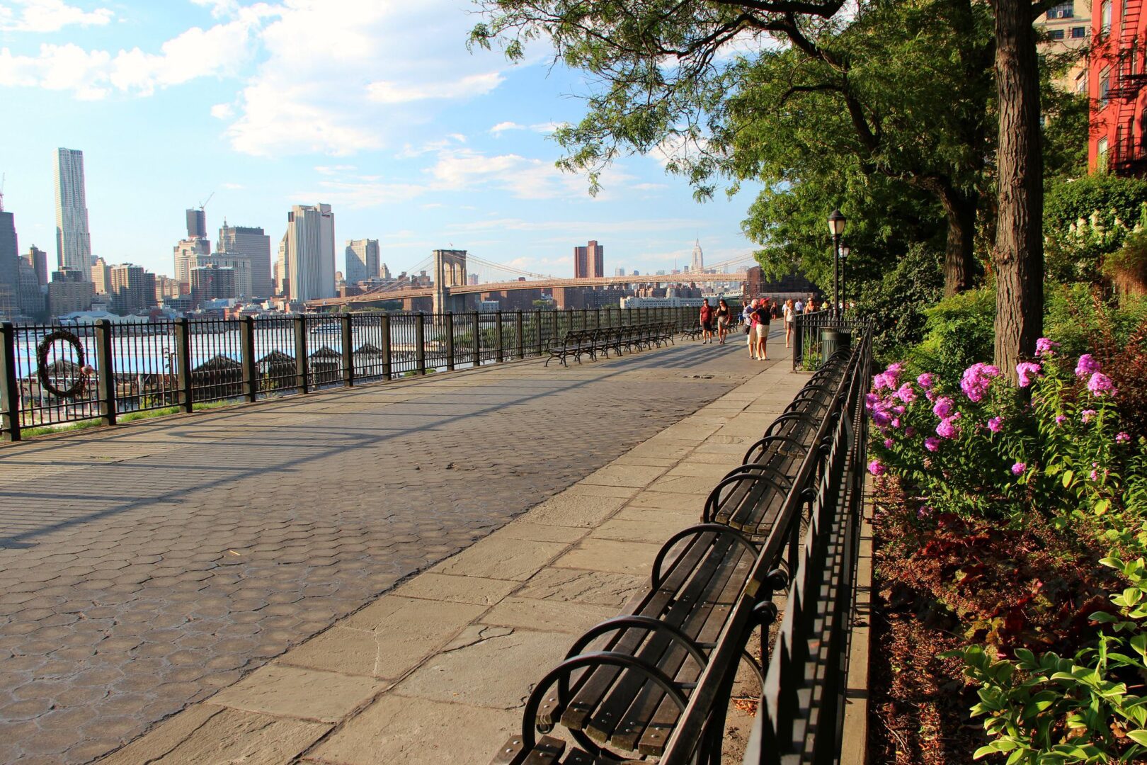 A scenic view of a waterfront promenade with benches overlooking a city skyline and bridge.