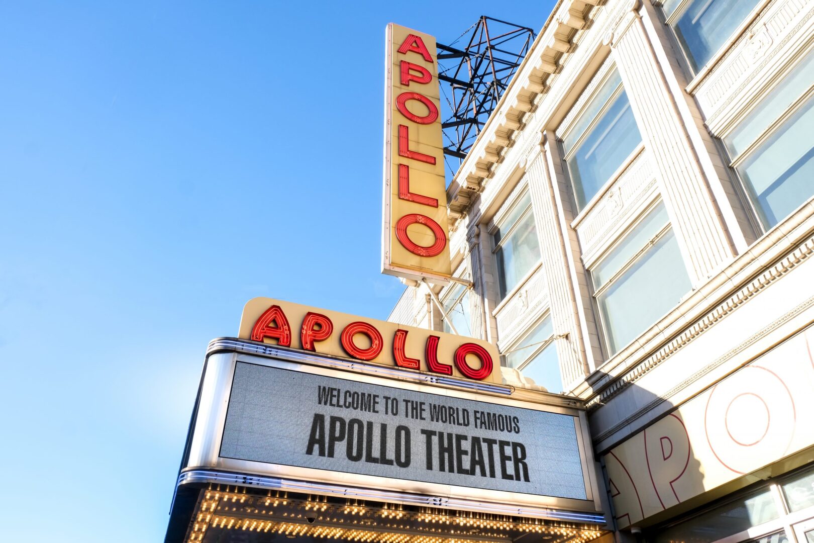 Marquee of the apollo theater welcoming visitors under a clear blue sky.