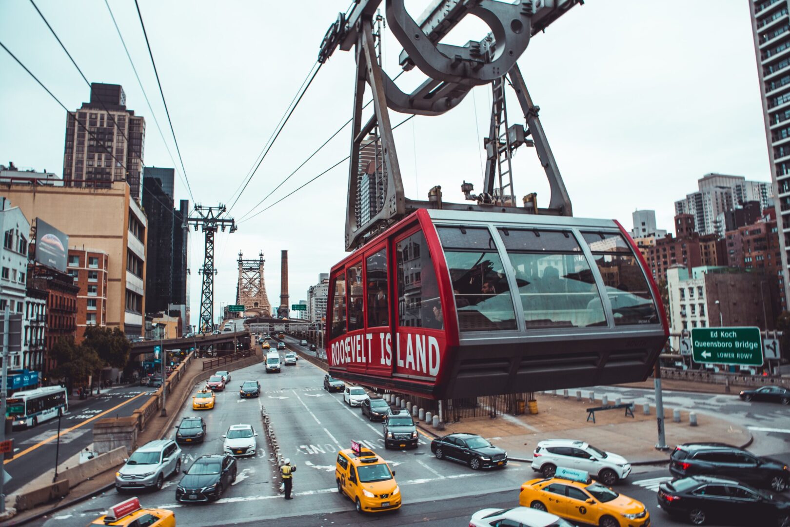 Roosevelt island tramway cabin gliding above busy city traffic.