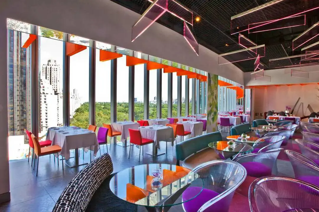 Luxury modern restaurant interior with vibrant color accents, floor-to-ceiling windows, and contemporary furniture.