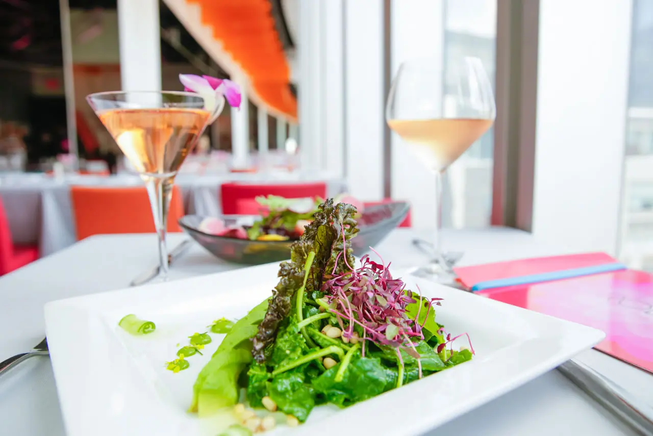 Luxury gourmet salad served on a white plate with a glass of rosé wine in a fine dining setting.
